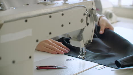 A-female-hand-pushes-material-through-a-sewing-machine